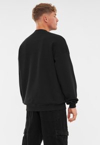 Svart sweatshirt med rund hals, avslappnad passform och ribbad mudd. Tillverkad av mjukt material, den har en slät yta utan synliga mönster.