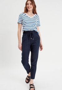 Haut à rayures à manches courtes en V blanc et bleu, associé à un pantalon tapered noir marine avec une taille élastique et un cordon de serrage, et des sandales noires.