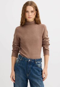 Suéter marrón de cuello alto de punto con puños acanalados, combinado con jeans de mezclilla azul de cintura alta, con cierre clásico de botones y bolsillos.