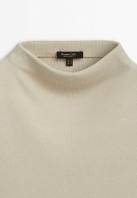 Beżowy sweter z prążkowanym kołnierzem, o gładkiej fakturze, miękkiej tkaninie i wysokim dekolcie. Posiada metkę z informacjami o marce i pielęgnacji.