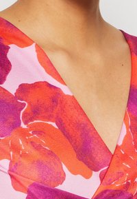 Gros plan sur une personne portant un vêtement à col en V avec un motif floral audacieux dans des tons rouges, violets et roses.