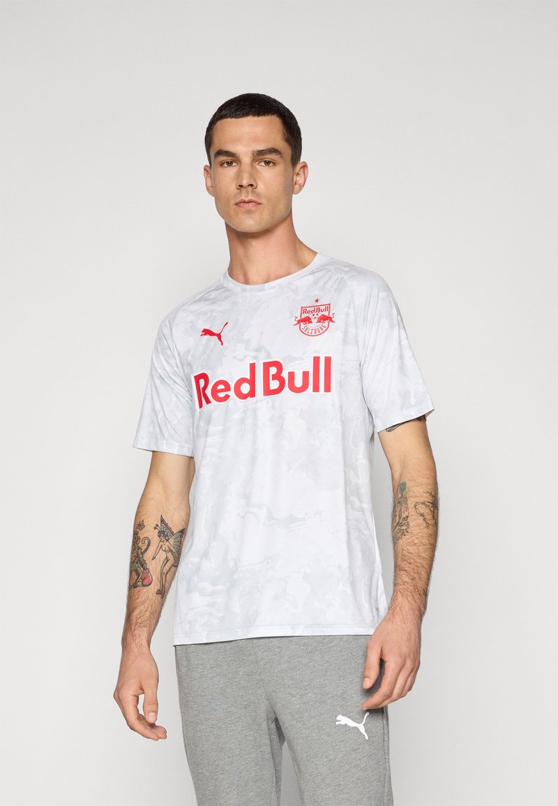 White camo-patterned short-sleeve shirt with red "Red Bull" text and logo. Made of a lightweight material; worn with grey sweatpants.