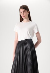 T-shirt en coton blanc associé à une jupe plissée noire avec une taille lisse et des plis verticaux, présentée dans un cadre minimaliste.