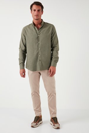 Cămașă verde cu guler și nasturi, pantaloni bej și adidași multicolori. Cămașa are un guler și nasturi, cu o textură netedă.