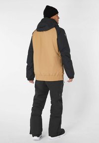 Herenjas met een zwart en bruin kleurenschema, een capuchon, elastische manchetten en een taille met een trekkoord, gecombineerd met zwarte broeken.