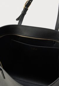 Melns ādas tote soma ar fakturētu virsmu, zelta rāvējslēdzēju un iekšējo kabatu ar reljefu logo. Ietverts regulējams siksniņa.