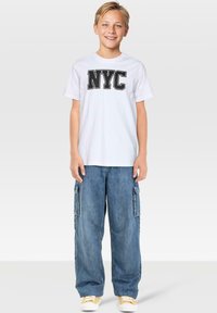 Vit bomullströja med svart "NYC"-tryck, kombinerad med ljusblå denim cargo-byxor med sidofickor och lös passform.