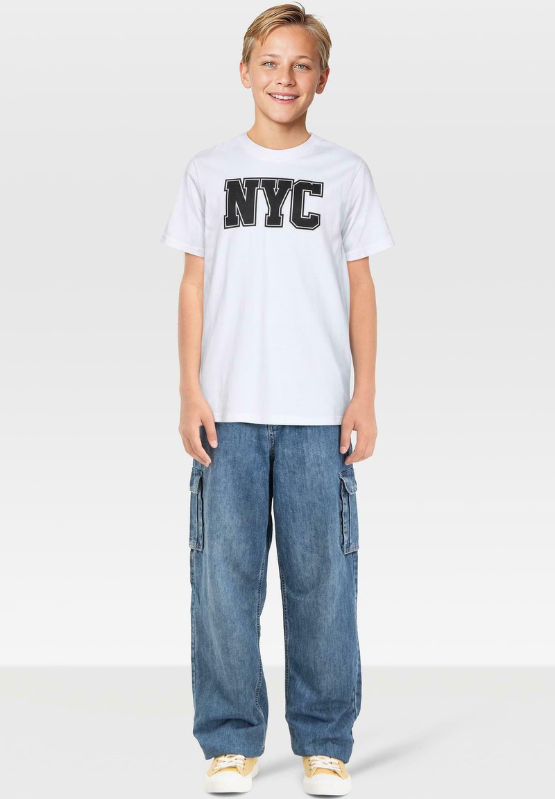 Vit bomullströja med svart "NYC"-tryck, kombinerad med ljusblå denim cargo-byxor med sidofickor och lös passform.