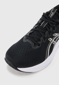 Scarpa sportiva nera con tomaia in mesh, lacci robusti e dettagli metallici. Presenta una soletta bianca e un battistrada testurizzato per migliorare la presa.