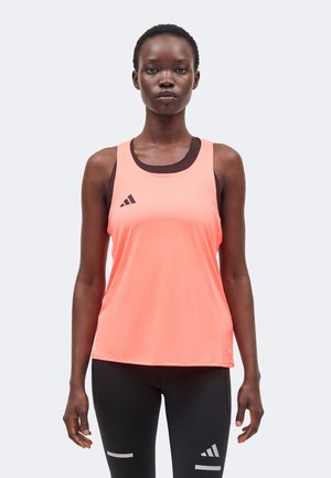 Frau mit kurzen Haaren, die ein korallenfarbenes ärmelloses Sporttop über einem schwarzen Sport-BH und schwarzen Leggings mit reflektierenden Streifen trägt.