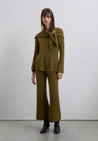 Olive green knitted two-piece set featuring a shawl collar top with a tie and flared pants; smooth texture with ribbed patterns.