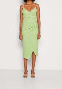 Grön, figurnära midiklänning med spaghettiband, inslagningdesign, rynkad textur och en sprund fram. Buren med nude öppen tåklack.
