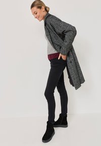 Túlméretezett szürke hounds-tooth kabát, szürke pulóver, amelyet bordó aláöltözetre rétegeztek, skinny fekete farmernadrág és fekete, szőrme díszítésű bokacsizma.