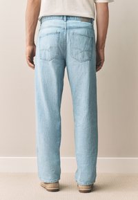 Jeans in denim azzurro chiaro con taglio dritto, due tasche posteriori e cuciture visibili. La vita presenta una toppa rettangolare in pelle.