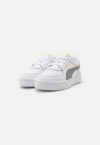 Vita sneakers med en slät läderövre, med grå detaljer, perforerad design, en tjock sula och en gul logotyp på plösen.