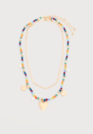 Collier à double rang avec une chaîne en or et un brin de perles colorées, comprenant un cœur en or, deux breloques coquillage, et de petites perles blanches.
