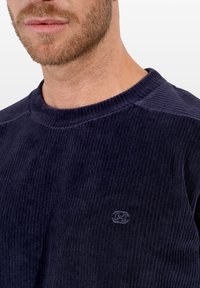 Sudadera de canalé en color navy, confeccionada en tejido suave, con un cuello redondo y un sutil logo en el pecho. Los detalles texturizados realzan el diseño.