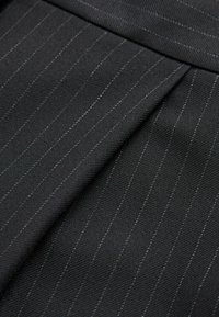 Tissu noir avec des rayures verticales en gris. La texture semble lisse avec un léger éclat. Présente des plis pliés pour un détail supplémentaire.