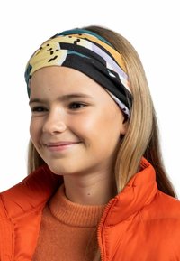 Multicolored headband featuring abstract patterns with yellow, black, and teal accents, worn with an orange puffer jacket and sweater.