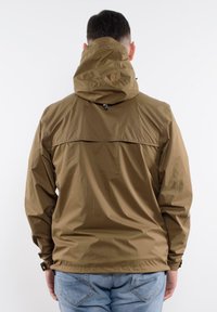 Brązowa wodoodporna kurtka z kapturem, o eleganckim kroju, z elastycznymi mankietami i kieszenią z tyłu. Nosi się ją na niebieskich dżinsach.