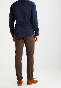 Navy long-sleeve shirt with a smooth texture, brown corduroy pants, and tan suede shoes, viewed from the back against a plain background.