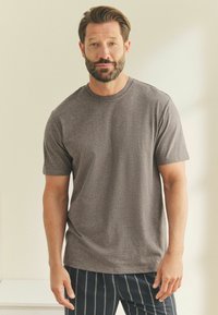 Kurzärmliges T-Shirt mit Rundhalsausschnitt in Dunkelgrau, aus weichem Stoff gefertigt. Hat eine lockere Passform mit glatter Textur. Wird mit gestreiften Hosen kombiniert.
