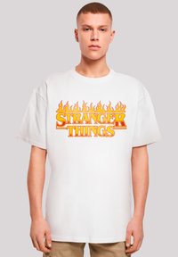 Weißes Baumwoll-T-Shirt mit auffälligem Design aus orangefarbenen und gelben Flammen um den Schriftzug "STRANGER THINGS", kurzen Ärmeln und einem lockeren Schnitt.