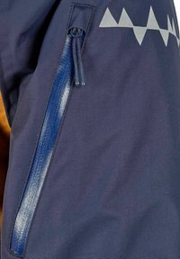 Nærbillede af en marineblå jakke med en lodret lynlåslomme, der har en struktureret blå vandtæt lynlås.