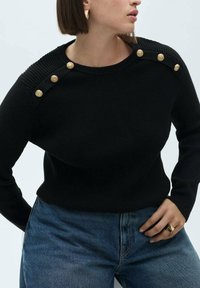 Maglione nero in maglia con spalle a coste, dotato di tre bottoni dorati. Abbinato a jeans in denim blu, che presentano una texture liscia e una forma aderente.