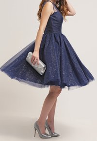 Navy blue cocktail dress with a fitted bodice, flared tulle skirt, and glitter accents. Paired with silver stiletto heels and clutch.