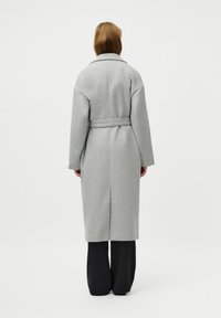 Cappotto grigio in lana con cintura, maniche ampie e uno spacco sul retro, caratterizzato da un colletto classico e un design di lunghezza media.