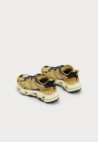 Zapatillas deportivas en tonos marrón y negro con una parte superior de malla, una amortiguación gruesa y una entresuela blanca contrastante. Cuenta con una suela exterior de goma texturizada.