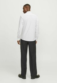 Camicia bianca a maniche lunghe con colletto, texture liscia e polsini con bottoni, abbinata a pantaloni neri e scarpe nere.