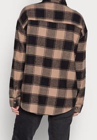 Rutig skjorta i beige och svart flanellmaterial, med knäppt krage, långa ärmar och rundad nederkant med sidoflikar.