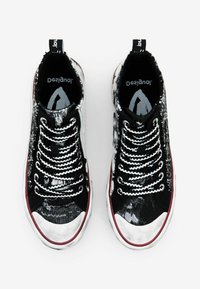 Baskets montantes en noir et blanc avec un motif, un dessus texturé, un embout en métal argenté, des lacets blancs et une semelle en caoutchouc rouge.