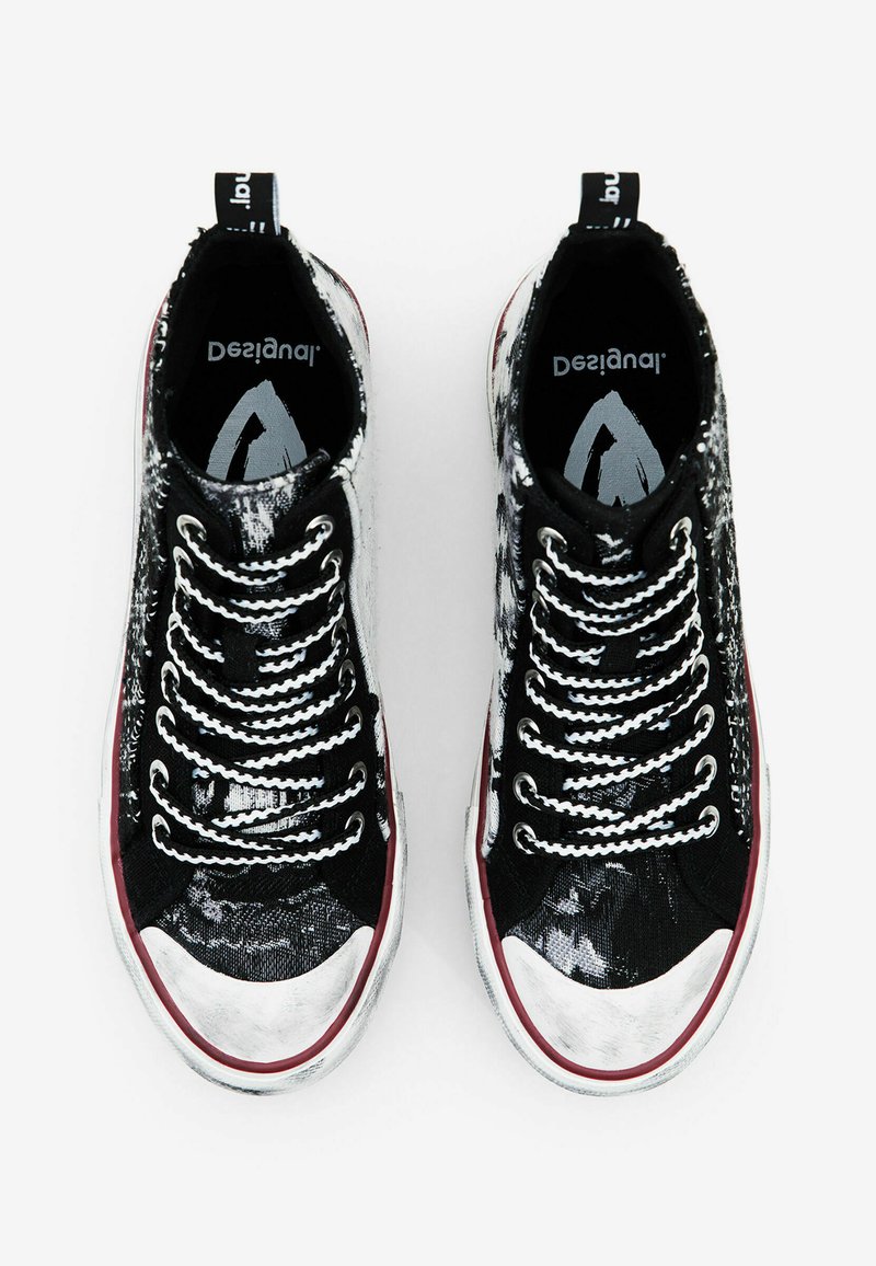 Zapatillas altas en blanco y negro con un diseño estampado, parte superior texturizada, puntera plateada, cordones blancos y suela de goma roja.