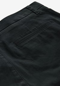 Schwarze Baumwollhose mit einer schlichten Gesäßtasche und einer glatten Stoffstruktur. Der Bund ist mit einem Gürtelbandschlaufe versehen.