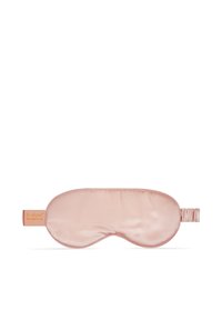 Masque de sommeil en soie rose clair avec bande élastique et petite étiquette marron sur le côté gauche.