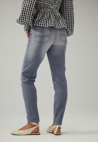 Jeans de denim de color azul claro con un diseño ajustado, cinco bolsillos y un leve desgastado; combinados con sandalias planas beiges con un diseño recortado.