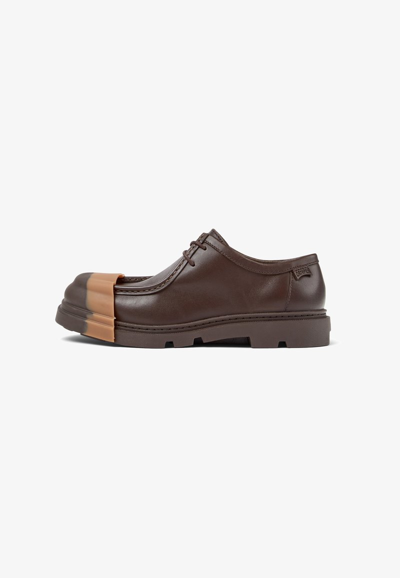 Chaussure en cuir marron avec une forme arrondie, protection en caoutchouc à l'avant et semelle épaisse. Présente un design à lacets et des accents minimalistes. Texture lisse.