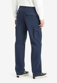 Navy cargo pants made of cotton, featuring multiple side pockets and a relaxed fit, paired with black high-top sneakers.