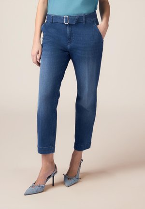 Pantalons en denim bleu cintrés avec une taille ceinturée, cinq poches et des poignets retroussés, associés à des chaussures à talons hauts bleu clair.