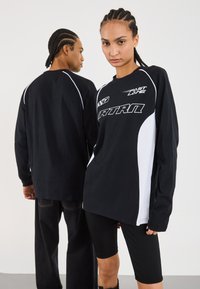 Black and white long-sleeve shirts featuring bold graphics, paired with black ribbed bike shorts. Smooth cotton texture, relaxed fit.