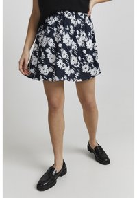 Blomstret nederdel i marineblå og hvid, lavet af letvægtsstof, har en samlet talje og en udvidet form, der når til midten af låret.