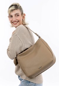 Sac à bandoulière en cuir beige avec une surface texturée, doté d'une seule bandoulière et d'un logo discret. Forme arrondie et accents lisses.