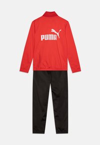 Ensemble de sport rouge comprenant une veste à col et un pantalon noir. Présente le logo blanc "PUMA" et l'emblème du chat au dos de la veste. Tissu lisse.