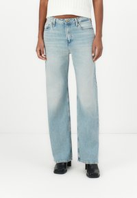 Jeans de tiro alto de mezclilla de color azul claro y pierna ancha, con cinco bolsillos y cierre de botón. Textura suave con un ligero desvanecimiento.