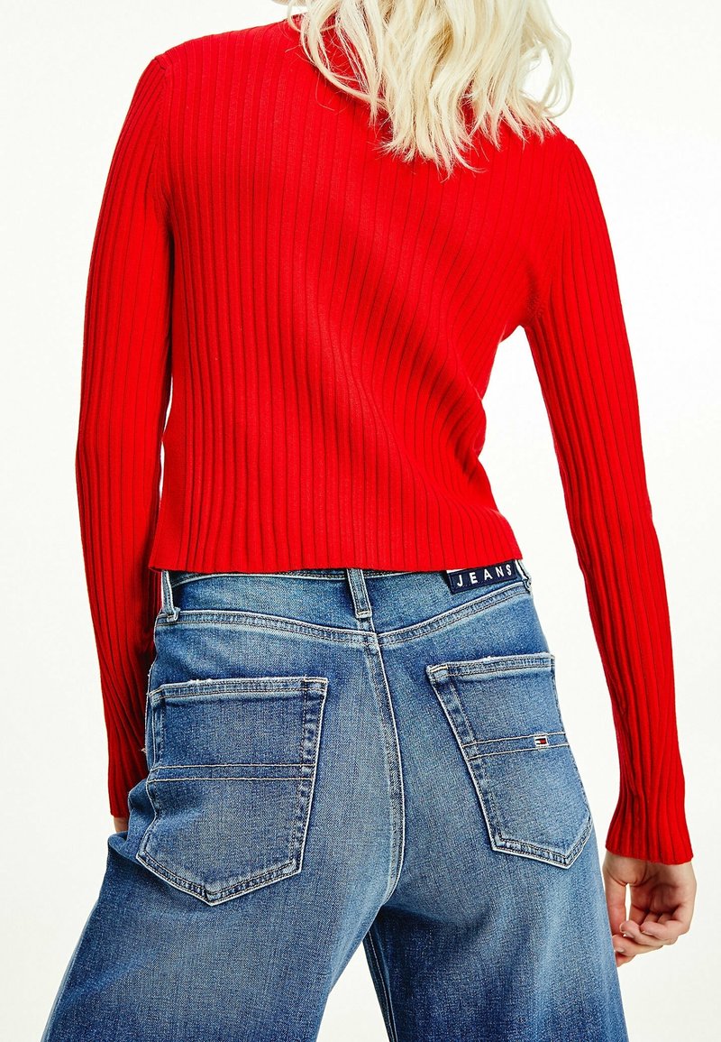 Rotes, geripptes Langarmoberteil, kombiniert mit blauen, hoch geschnittenen Jeans mit zwei Gesäßtaschen und einem Markenlabel am Bund.