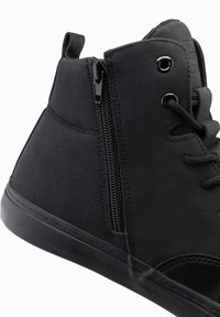 Černé semišové kotníkové boty mají šněrovací design, boční zip a strukturovaný povrch s gumovou podrážkou a černými očky.