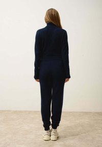 Mörkblå, stickad jumpsuit med hög krage och långa ärmar. Har ribbade manschetter och midja. Bärs med beige sneakers.